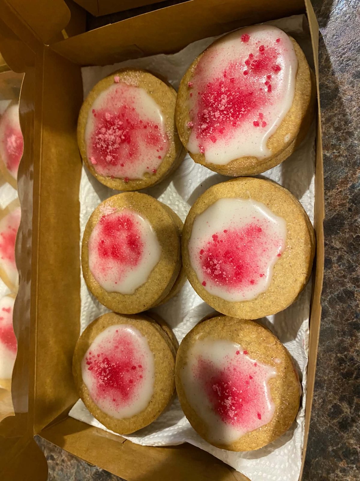Six small iced bakes with pink sprinkles in a kraft box.